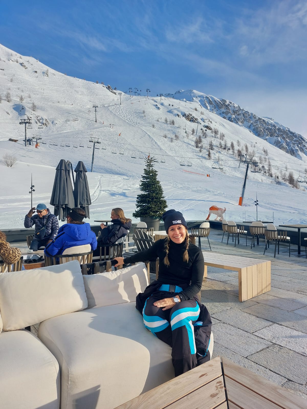 Celeste Miranda em estação de ski, com picos nevados e teleféricos ao fundo